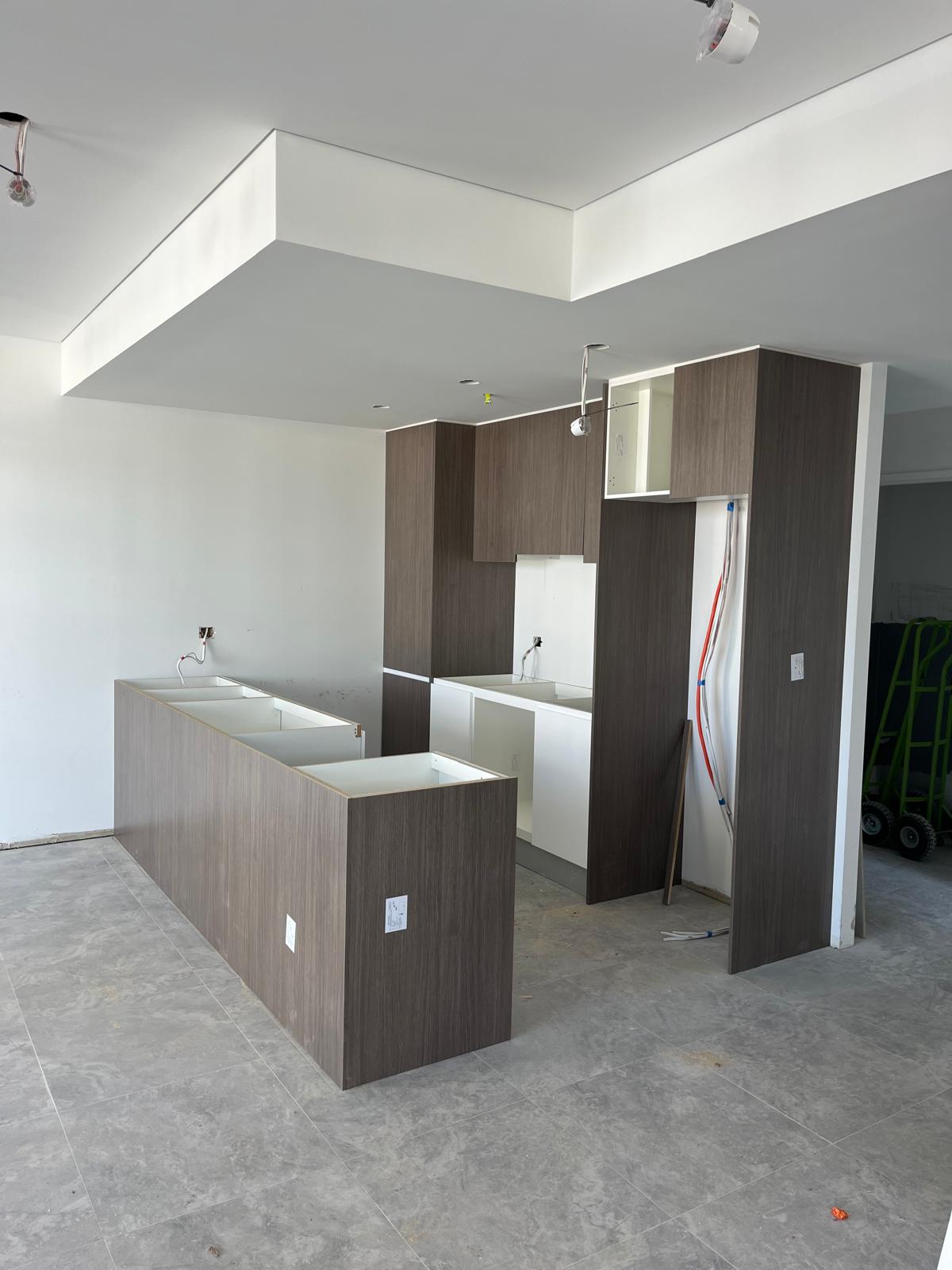 Pose cuisine Sydney — façades bois foncé sur îlot central et caissons, meubles hauts en cours, vue 1