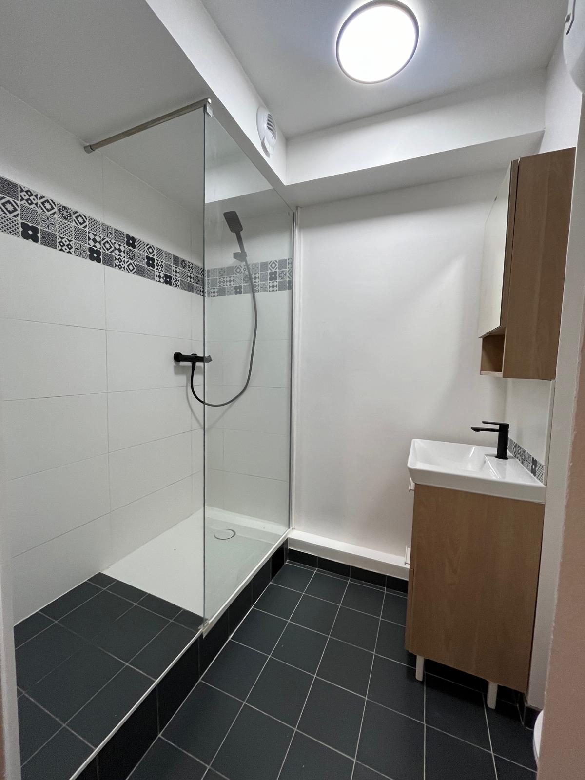 Salle de bain rénovée dans un studio locatif à Noisy-le-Grand — douche avec paroi vitrée et carrelage gris anthracite